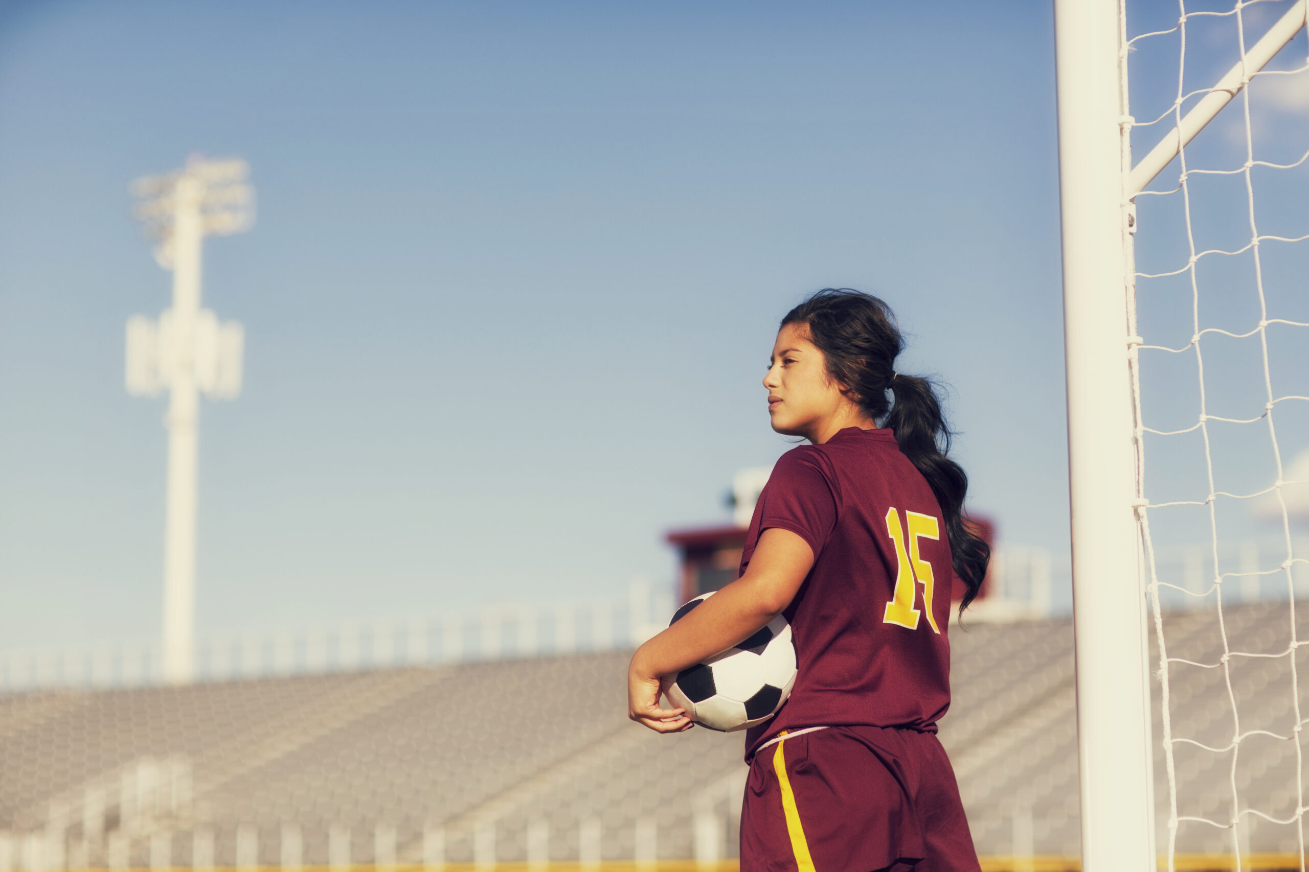 A woman standing on a grass field with a football in her lap.